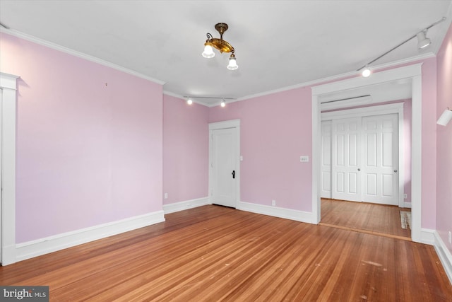 unfurnished bedroom with wood finished floors, baseboards, ornamental molding, and track lighting