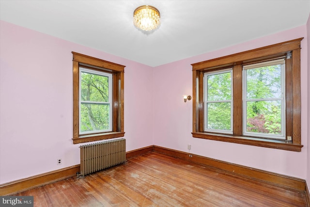 unfurnished room featuring a chandelier, light wood-type flooring, radiator heating unit, and baseboards