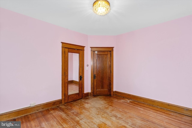 empty room featuring light wood-style flooring, a notable chandelier, and baseboards