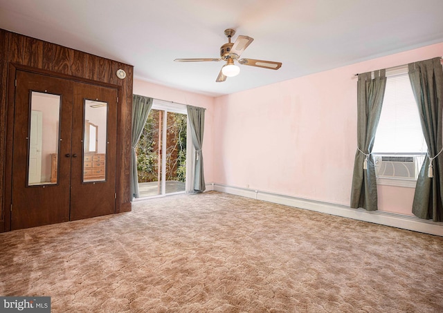 interior space featuring a baseboard heating unit, ceiling fan, carpet floors, and wood walls