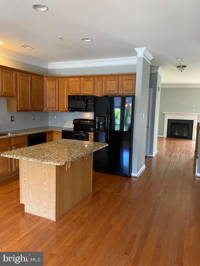 kitchen with a kitchen island, hardwood / wood-style flooring, black appliances, crown molding, and light stone counters