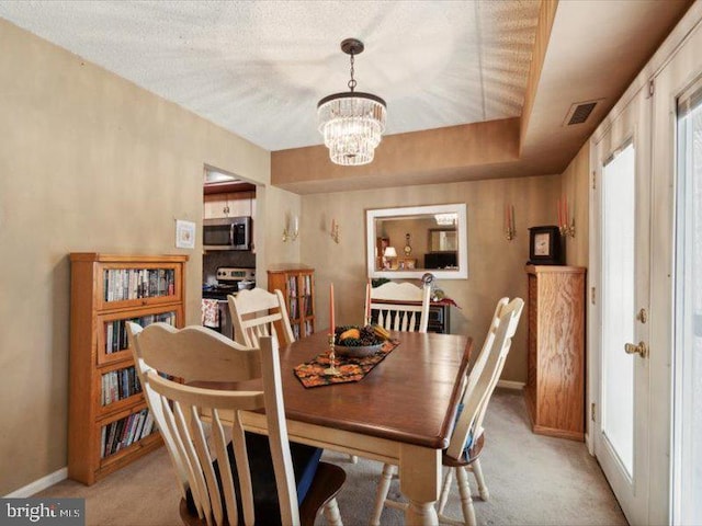 carpeted dining area with a tray ceiling, a textured ceiling, and an inviting chandelier