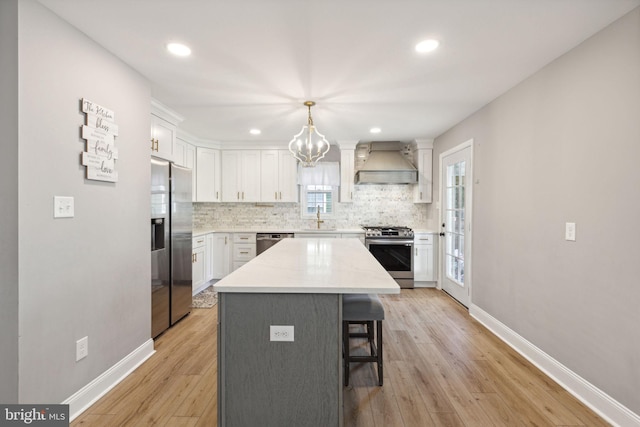 kitchen with light hardwood / wood-style floors, a kitchen island, custom range hood, decorative light fixtures, and stainless steel appliances