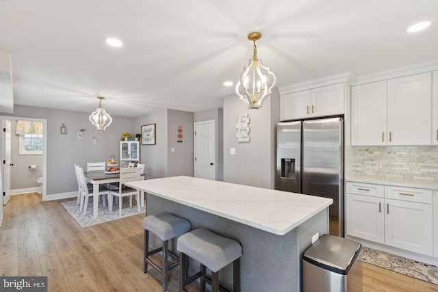 kitchen featuring white cabinets, hanging light fixtures, light wood-type flooring, and stainless steel fridge