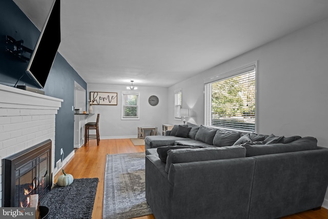 living room with light wood-type flooring, a fireplace, baseboards, and a chandelier