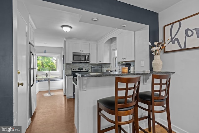 kitchen with stainless steel appliances, wood finished floors, white cabinets, and dark countertops
