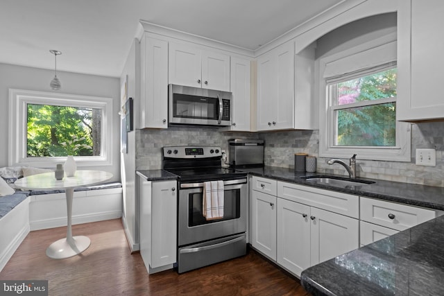 kitchen featuring stainless steel appliances, a sink, white cabinetry, dark wood finished floors, and dark stone counters