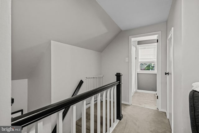 corridor with an upstairs landing, lofted ceiling, light carpet, and baseboards