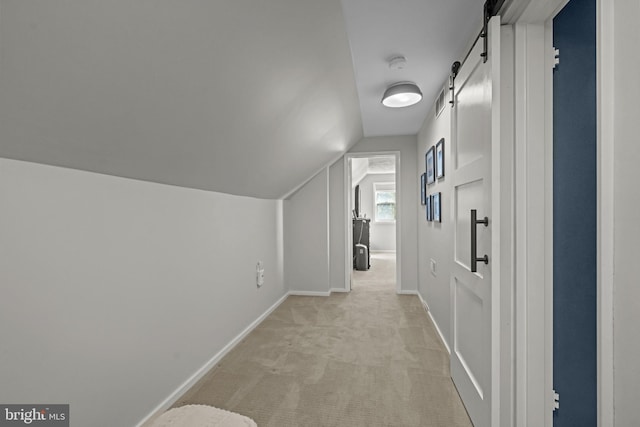 corridor with lofted ceiling, light carpet, a barn door, and baseboards