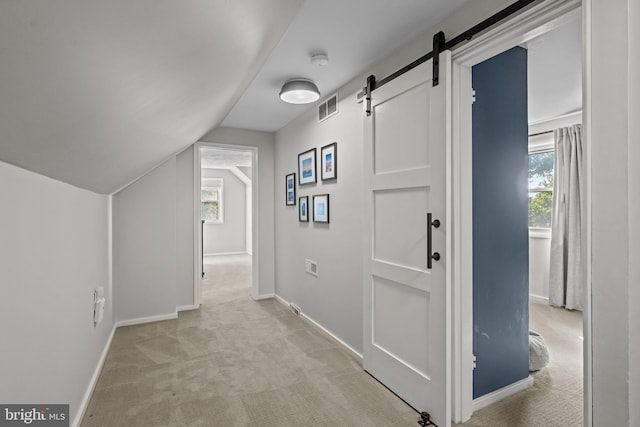 hall with light colored carpet, a barn door, baseboards, healthy amount of natural light, and vaulted ceiling