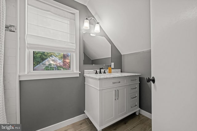 full bath with baseboards, vanity, wood finished floors, and vaulted ceiling