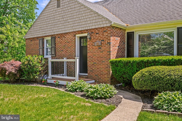 property entrance with brick siding, a lawn, and a shingled roof