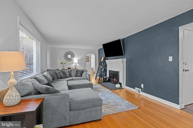 living area with arched walkways, wood finished floors, a lit fireplace, and baseboards