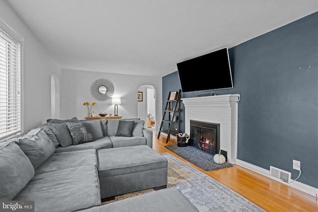 living area featuring arched walkways, wood finished floors, a brick fireplace, and baseboards