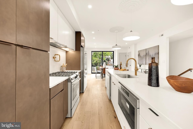 kitchen featuring appliances with stainless steel finishes, white cabinets, light hardwood / wood-style flooring, and pendant lighting