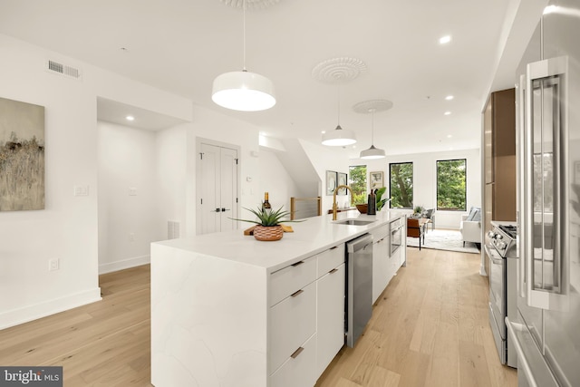 kitchen with white cabinets, a center island with sink, light hardwood / wood-style flooring, sink, and decorative light fixtures