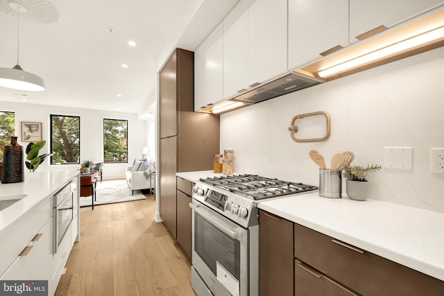 kitchen with high end stainless steel range, dark brown cabinetry, decorative light fixtures, light wood-type flooring, and white cabinetry