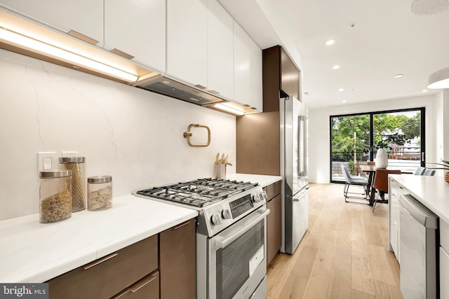 kitchen with dark brown cabinetry, white cabinetry, appliances with stainless steel finishes, light stone counters, and light hardwood / wood-style floors