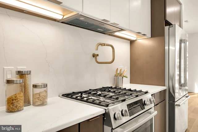 kitchen featuring dark brown cabinets, stainless steel appliances, light stone countertops, white cabinetry, and light hardwood / wood-style floors