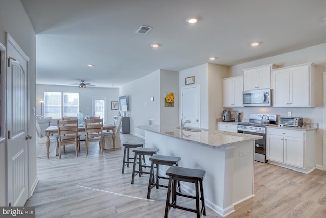 kitchen with sink, appliances with stainless steel finishes, white cabinets, and an island with sink