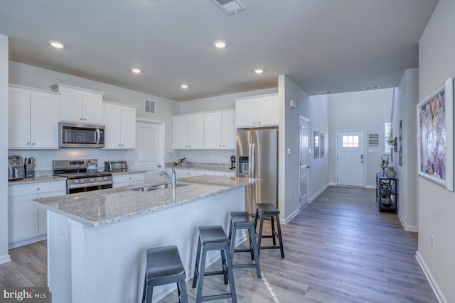 kitchen with appliances with stainless steel finishes, sink, white cabinetry, light hardwood / wood-style floors, and a center island with sink