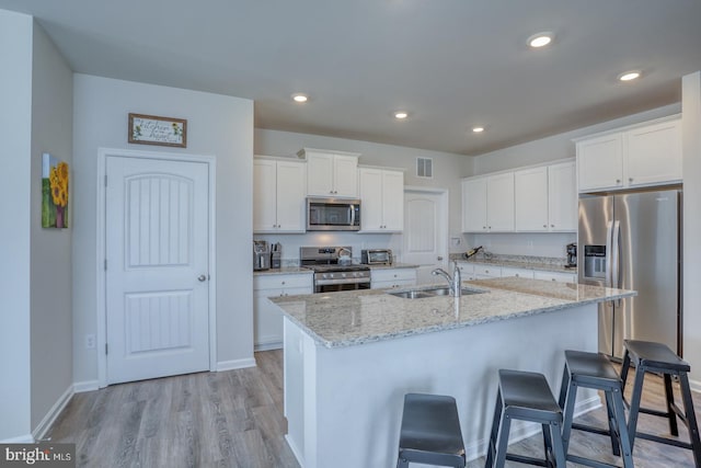 kitchen with light hardwood / wood-style flooring, a center island with sink, sink, white cabinetry, and appliances with stainless steel finishes