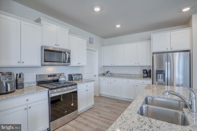 kitchen with stainless steel appliances, sink, light wood-type flooring, white cabinets, and light stone counters