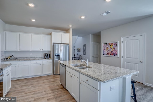 kitchen with white cabinets, a center island with sink, stainless steel appliances, light hardwood / wood-style floors, and sink