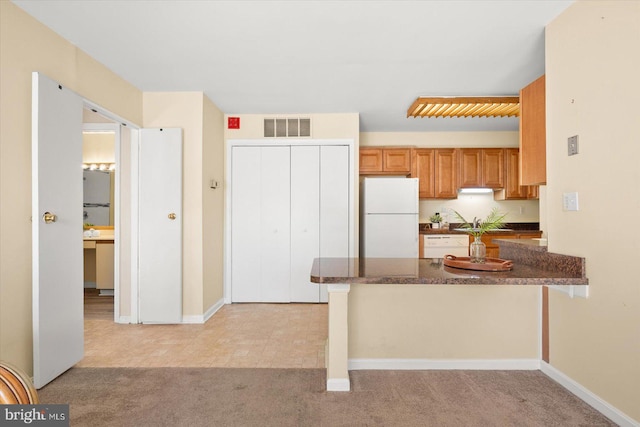 kitchen with a kitchen breakfast bar, kitchen peninsula, light carpet, sink, and white refrigerator