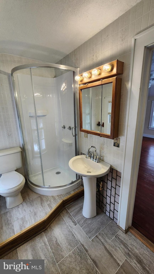 bathroom featuring toilet, an enclosed shower, tile walls, and a textured ceiling