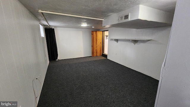 basement featuring dark carpet, a textured ceiling, and wood walls