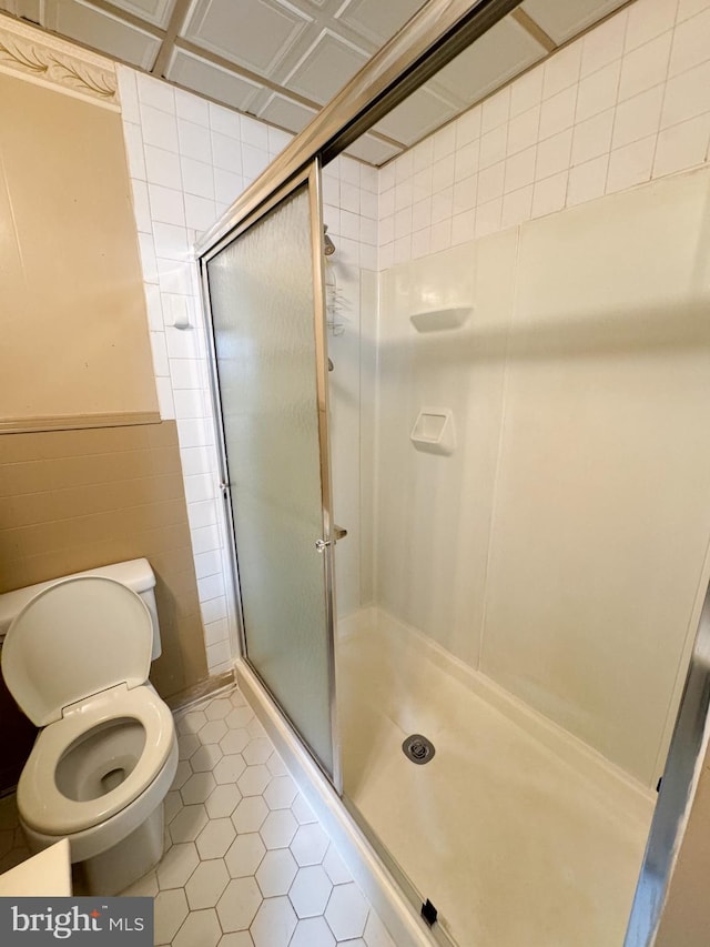 bathroom featuring tile walls, tile patterned floors, toilet, and an enclosed shower