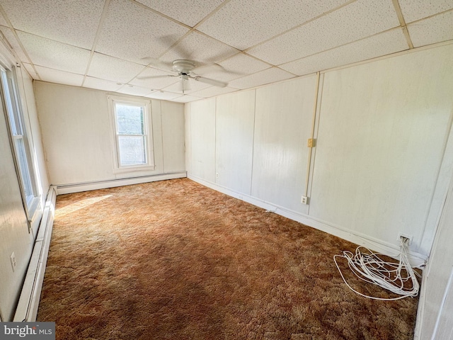 empty room with baseboard heating, a drop ceiling, carpet floors, and ceiling fan