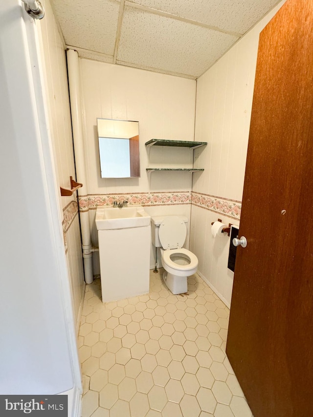 bathroom with sink, a drop ceiling, toilet, and tile patterned flooring