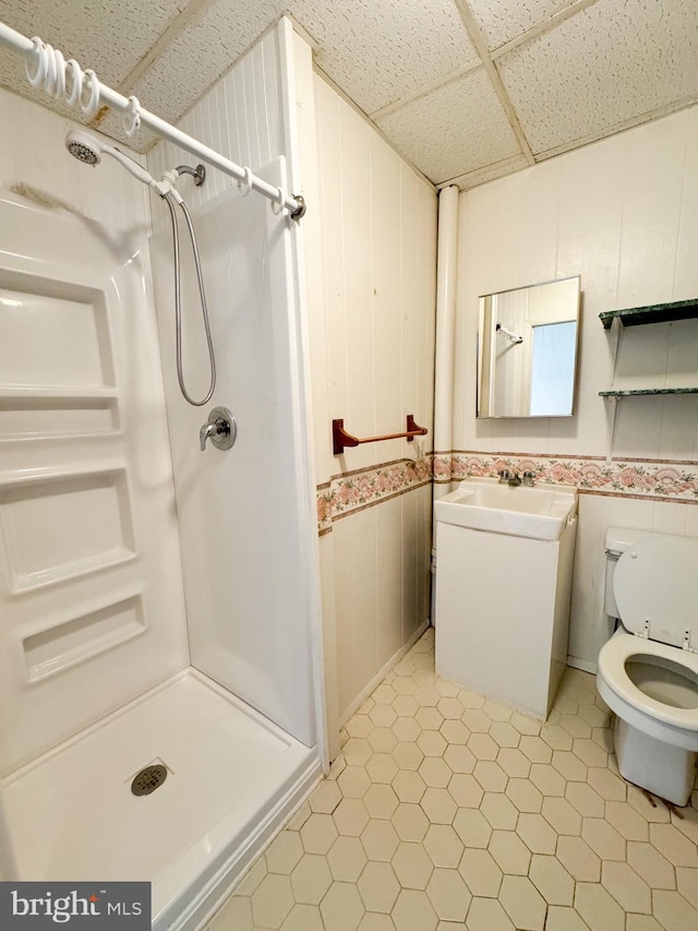 bathroom featuring toilet, tile patterned flooring, wooden walls, a shower, and a paneled ceiling