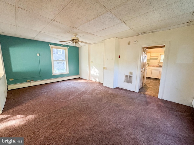 empty room with baseboard heating, carpet, a paneled ceiling, and ceiling fan