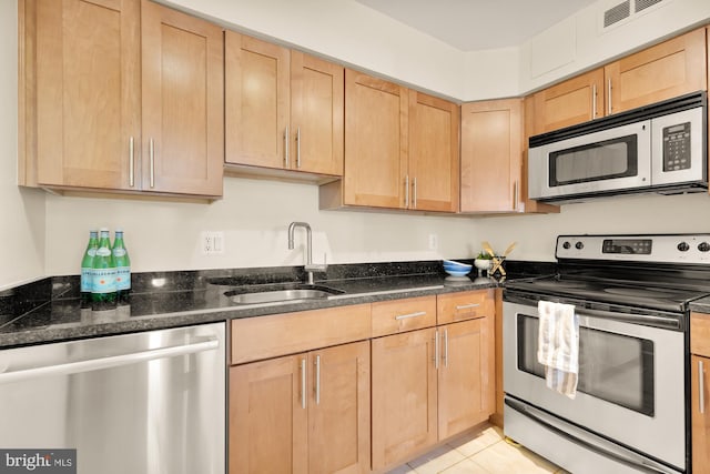 kitchen with dark stone countertops, light brown cabinets, sink, appliances with stainless steel finishes, and light tile patterned floors