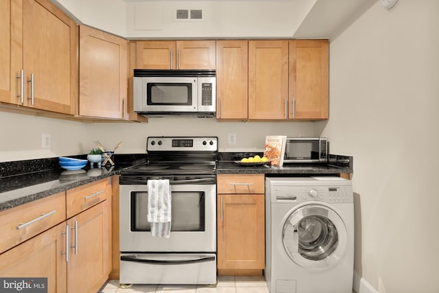 kitchen with light tile patterned floors, appliances with stainless steel finishes, washer / dryer, light brown cabinetry, and dark stone counters