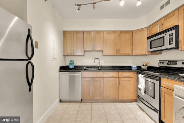 kitchen with stainless steel appliances, dark stone counters, light tile patterned flooring, and sink