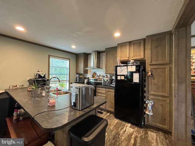 kitchen with wall chimney range hood, black fridge, a kitchen bar, dark wood-type flooring, and sink