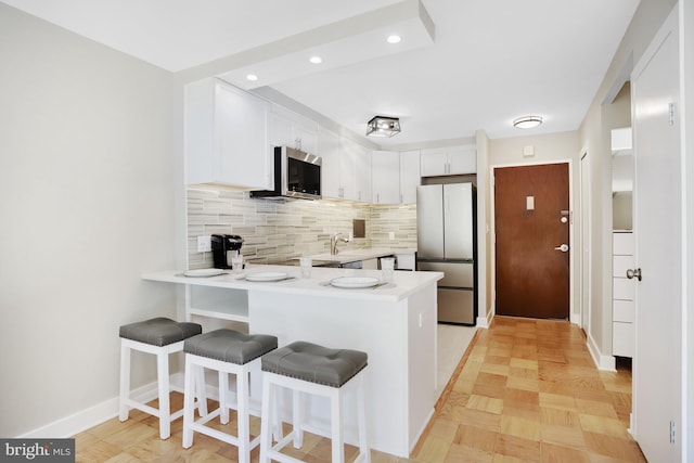 kitchen with light hardwood / wood-style floors, kitchen peninsula, white cabinetry, a breakfast bar area, and appliances with stainless steel finishes