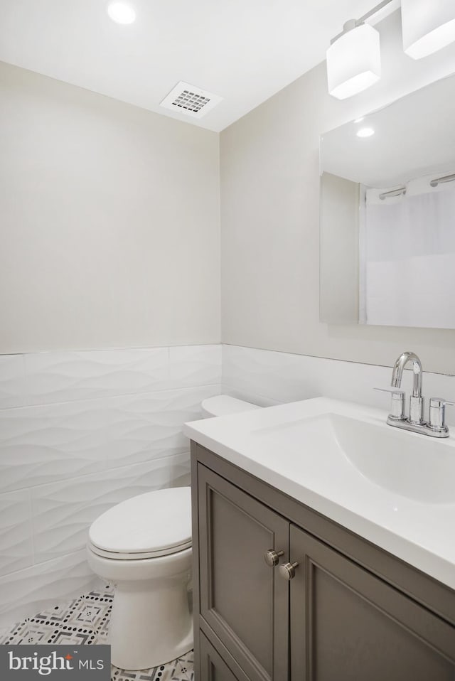 bathroom featuring tile patterned flooring, vanity, tile walls, and toilet