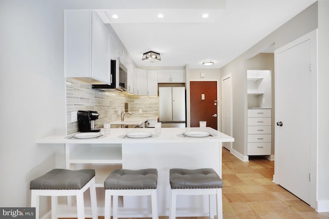 kitchen featuring light wood-type flooring, a breakfast bar, kitchen peninsula, white cabinets, and white fridge