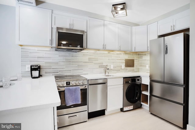 kitchen with washer / dryer, decorative backsplash, sink, white cabinetry, and appliances with stainless steel finishes