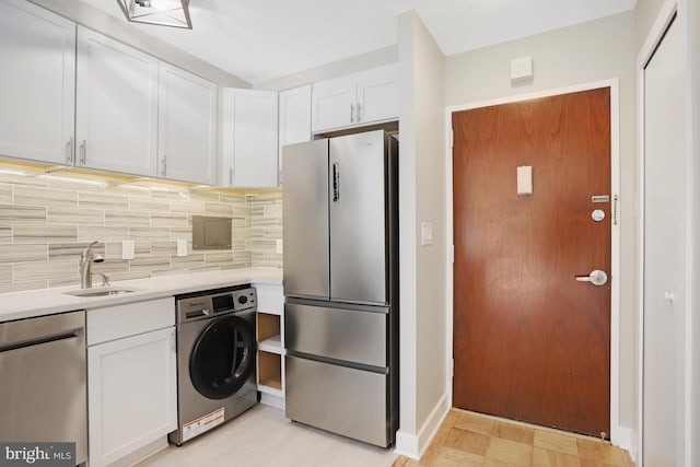 kitchen with tasteful backsplash, sink, stainless steel appliances, washer / clothes dryer, and white cabinets