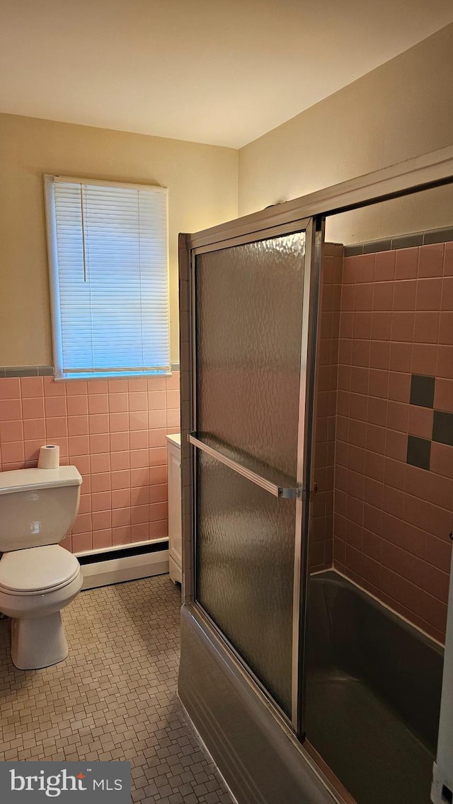 bathroom featuring toilet, tile patterned flooring, baseboard heating, tile walls, and enclosed tub / shower combo