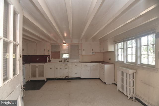 kitchen featuring beamed ceiling, sink, radiator heating unit, and white cabinetry