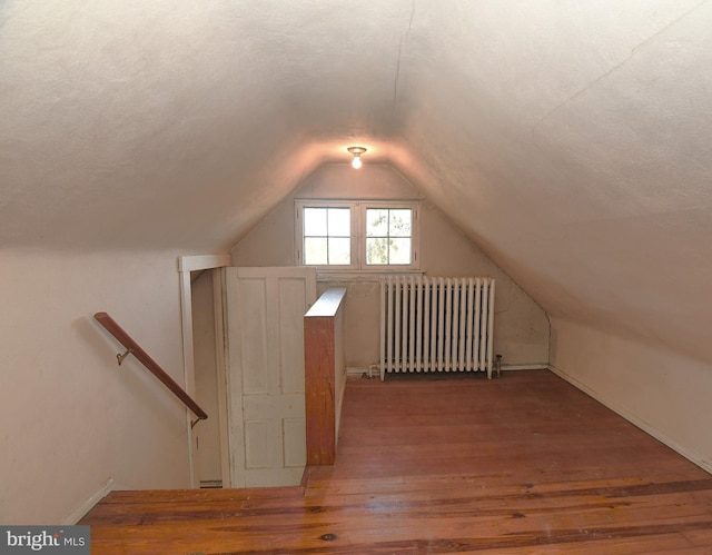 additional living space with wood-type flooring, radiator, a textured ceiling, and vaulted ceiling