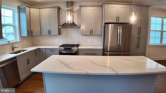 kitchen with stainless steel appliances, a wealth of natural light, wall chimney range hood, and decorative light fixtures