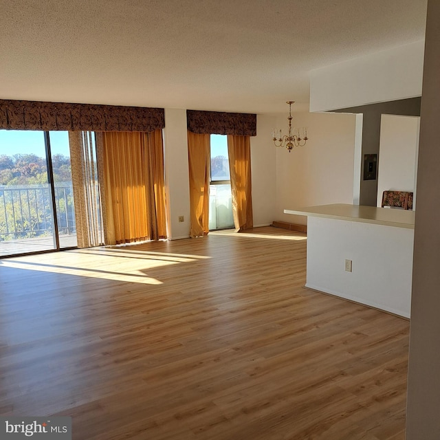 unfurnished living room featuring a chandelier, wood-type flooring, and a textured ceiling